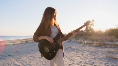 Sahilin yanındaki doğada bas gitar çalan bir kız..