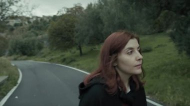 Bulutlu bir günde kırsalda pelerinli genç bir kadın..