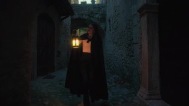 Gizemli genç kadın pelerin ve fenerle bir köyün sokaklarında yürüyor..
