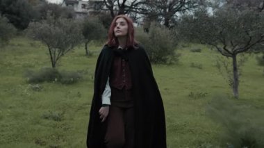 Bulutlu bir günde kırsalda pelerinli genç bir kadın..