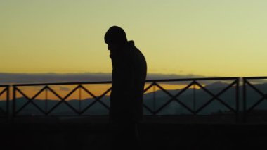 Sinirli ve sinirli bir adamın silueti telefonda konuşuyor, Sunset 'te balkonda..