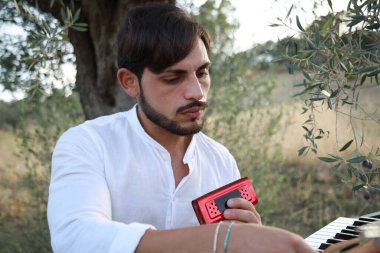 Beyaz gömlekli çocuk dışarıdaki doğada piyano çalıyor..