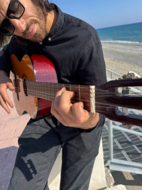 Uzun Saçlı Çocuk Yazın Okyanusta Siyah Giyinik Klasik Gitar Çalıyor.