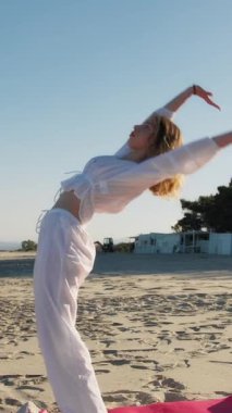 Yazın plajda beyazlar içinde dans eden genç bir kadın.