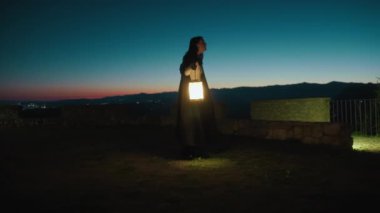 Gizemli genç kadın pelerin ve fenerle bir köyün sokaklarında yürüyor..