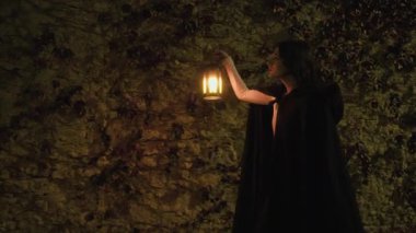 Gizemli genç kadın pelerin ve fenerle bir köyün sokaklarında yürüyor..
