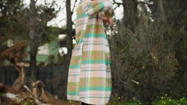 Ekose gömlekli kadın parkta ağaçların önünde yavaşça dans ediyor..