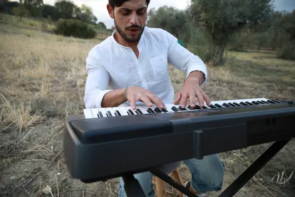 Beyaz gömlekli çocuk dışarıdaki doğada piyano çalıyor..