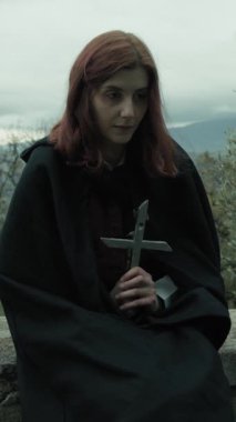 Bulutlu bir günde kırsalda pelerinli genç bir kadın..