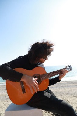 Adam yazın deniz kenarındaki sahilde klasik gitar çalıyor..