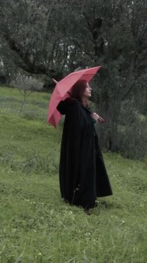 Bulutlu bir günde kırsalda pelerinli genç bir kadın..