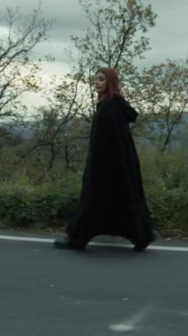 Bulutlu bir günde kırsalda pelerinli genç bir kadın..