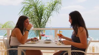 İki kadın yemek yerken içki içiyor. . 