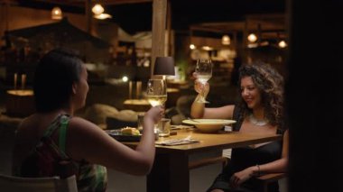 Lüks oteldeki bir akşam yemeğinde iki kadın bir bardak şarapla tezahürat yapıyor. .