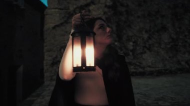 Gizemli genç kadın pelerin ve fenerle bir köyün sokaklarında yürüyor..