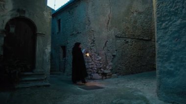 Gizemli genç kadın pelerin ve fenerle bir köyün sokaklarında yürüyor..