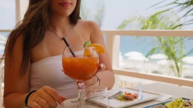 Saçında rüzgarla portakal kokteyli içen bir kadın. . 
