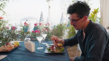 Sahilde öğle yemeği yerken deniz manzarasına hayran olan bir adam. . 