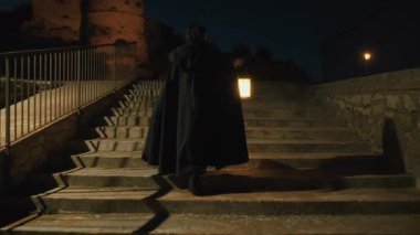 Gizemli genç kadın pelerin ve fenerle bir köyün sokaklarında yürüyor..
