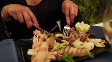 Yemek sırasında ızgara balık aperatifi yemek için çatal kullanan bir kadın. .