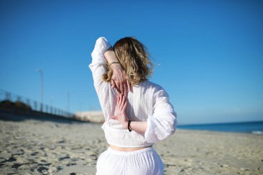 Beyaz tişörtlü bir kızın sırtı okyanusun kıyısındaki kumsalda uzanıyor. .