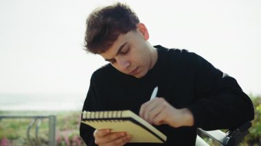 Adam, parktaki bankta kalemle not defterine fikir yazıyor. . 