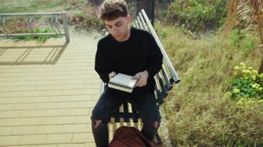 Adam parkta defterini kapatıp sırt çantasına koyuyor. . 