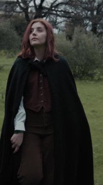 Bulutlu bir günde kırsalda pelerinli genç bir kadın..