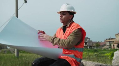 İnşaat işçisi proje belgesine bakıyor. . 