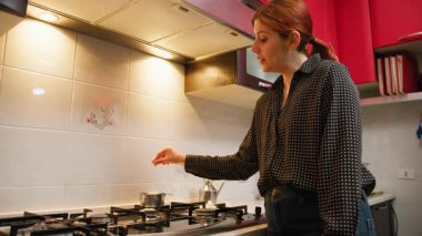 Küçük bir mutfakta bir kadın çay poşetini tavaya batırır..