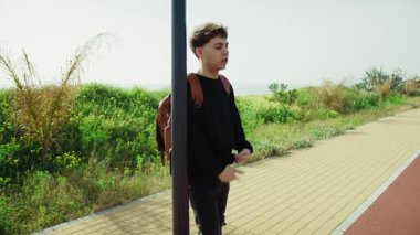 Kaldırımda sırt çantalı bir adam otobüsün gelmesini bekliyor. . 