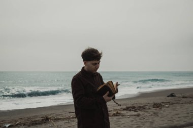 Okyanusun kenarında dua eden bir adam İncil 'in sayfalarını çeviriyor. . 