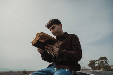 Hıristiyan adam sahildeyken İncil 'de dua okuyor. . 