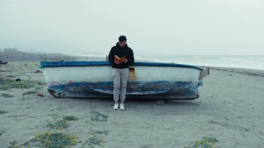 Adam kasvetli bir günde deniz kenarında yalnızlık içinde kitap okuyor.. 