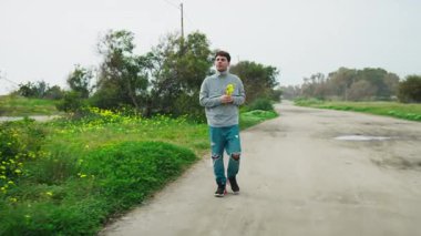 Doğadaki adam elinde sarı çiçeklerle yürüyor.. 