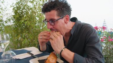 Adam sahildeki restoranda öğle yemeğinde hamburgerin tadını çıkarıyor. . 