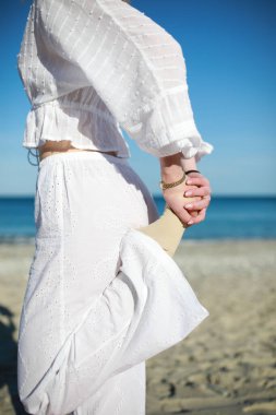 Beyazlar içinde genç bir kadın sahile yakın bir yerde egzersiz yapıyor. 