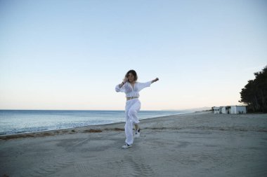 Yazın gün batımında sahilin kenarında beyaz giysili hip hop dansçısı kız. .