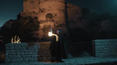 Gizemli genç kadın pelerin ve fenerle bir köyün sokaklarında yürüyor..