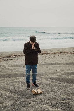 Okyanusun kenarında dua eden bir adam İncil 'in sayfalarını çeviriyor. . 