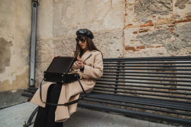 Bankta oturan bir kadın eski model kamerayla çantayı açıyor. . 