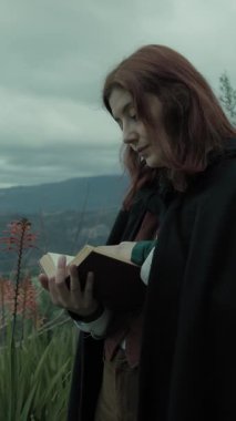 Bulutlu bir günde kırsalda pelerinli genç bir kadın..