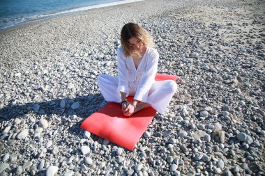 Beyazlar içindeki kız sahile yakın bir yerde yoga yapıyor mu? .
