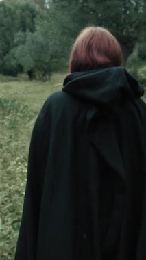 Bulutlu bir günde kırsalda pelerinli genç bir kadın..