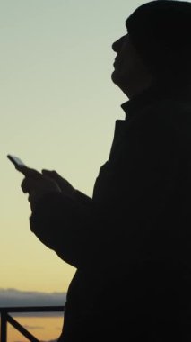 Gün batımında akıllı telefonuyla fotoğraf çeken bir adamın silueti..