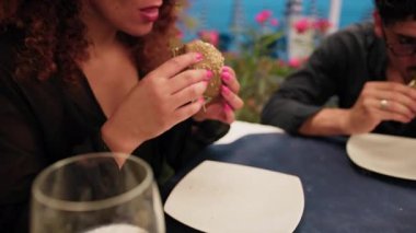 Sahildeki restoranda akşam yemeği sırasında gurme balık burgerinin yarısını yiyen bir kadın. .