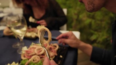 Restoranda romantik bir akşam yemeğinde kızarmış mürekkep balığı yiyen adam. .