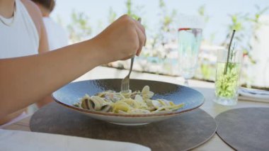 Bir kadın, sahilde öğle yemeğinde spagetti yemek için çatalı döndürüyor. .