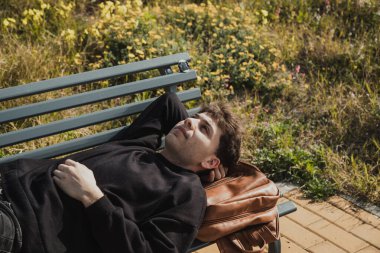 Yorgun adam dışarıda bankta sırt çantasında uyuyor. . 