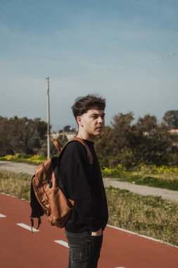 Kaldırımda sırt çantalı bir adam otobüsün gelmesini bekliyor. . 